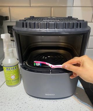 A Cosori air fryer turned upside down and cleaned with an old pink toothbrush with Mrs. Meyer's multi surface cleaner