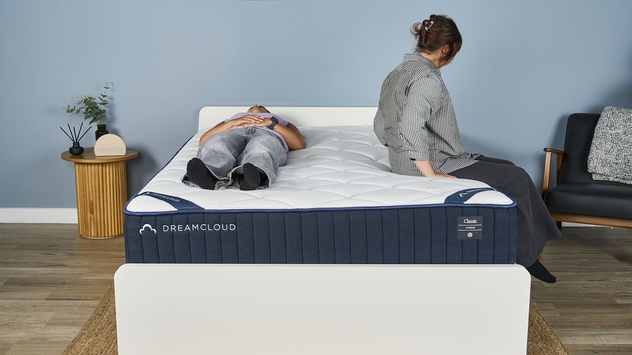 One Tom's Guide tester lies on her back on the DreamCloud Classic inside a blue-painted bedroom while another gets into bed, lies on her side and then lies on her other side