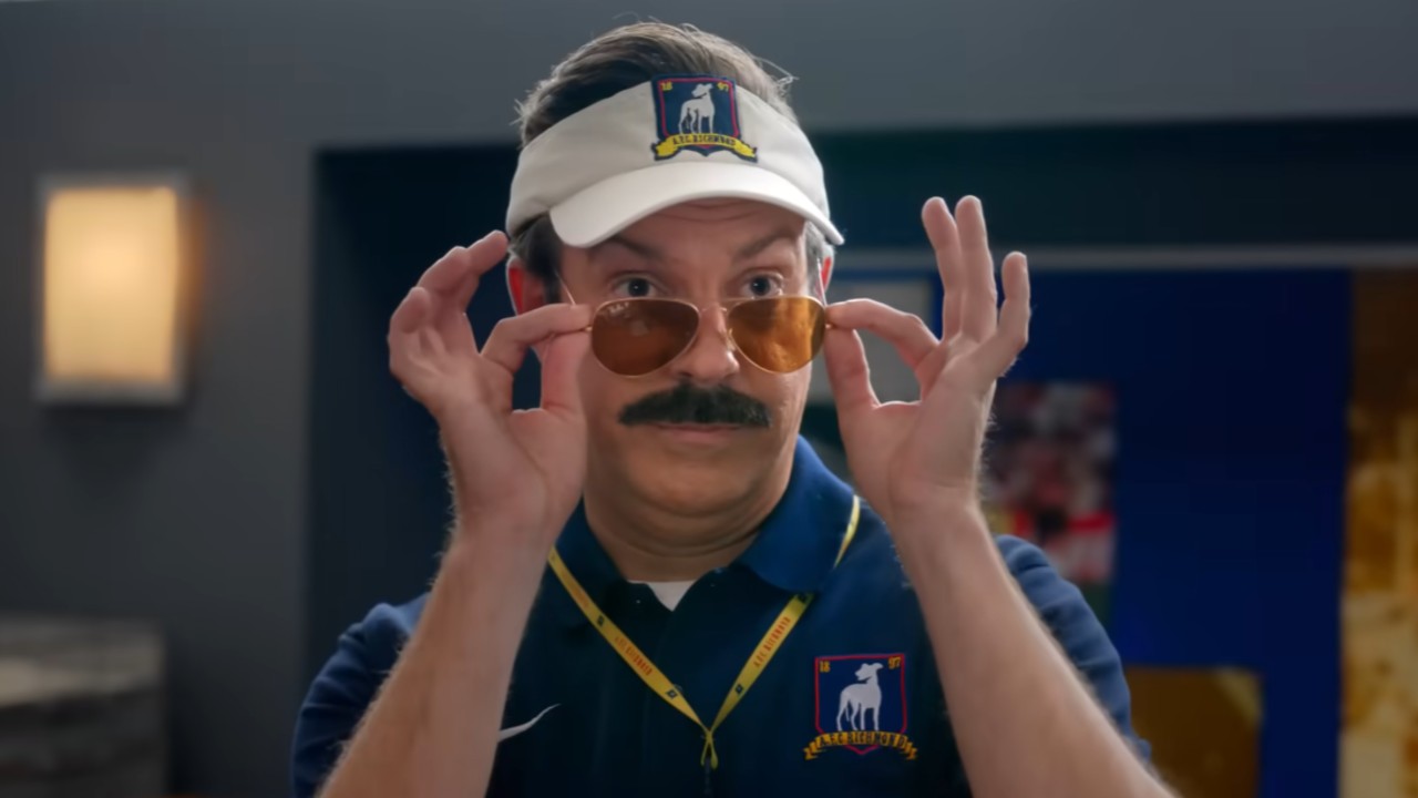 Ted pulling down his sunglasses with both his hands and peering over them in Ted Lasso Season 4. 