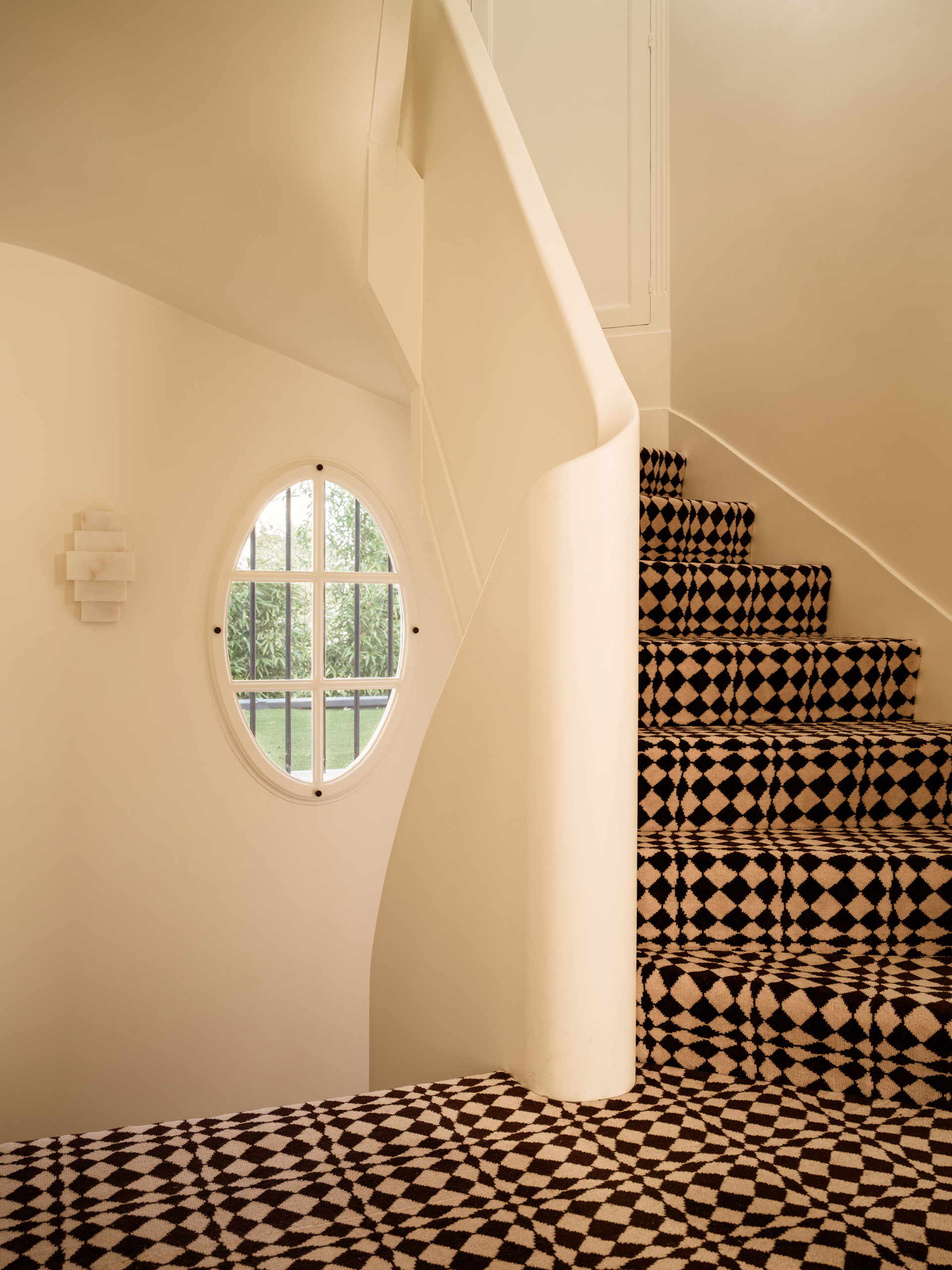 Curved staircase with cream walls and black and beige geometric patterned carpet and a porthole window