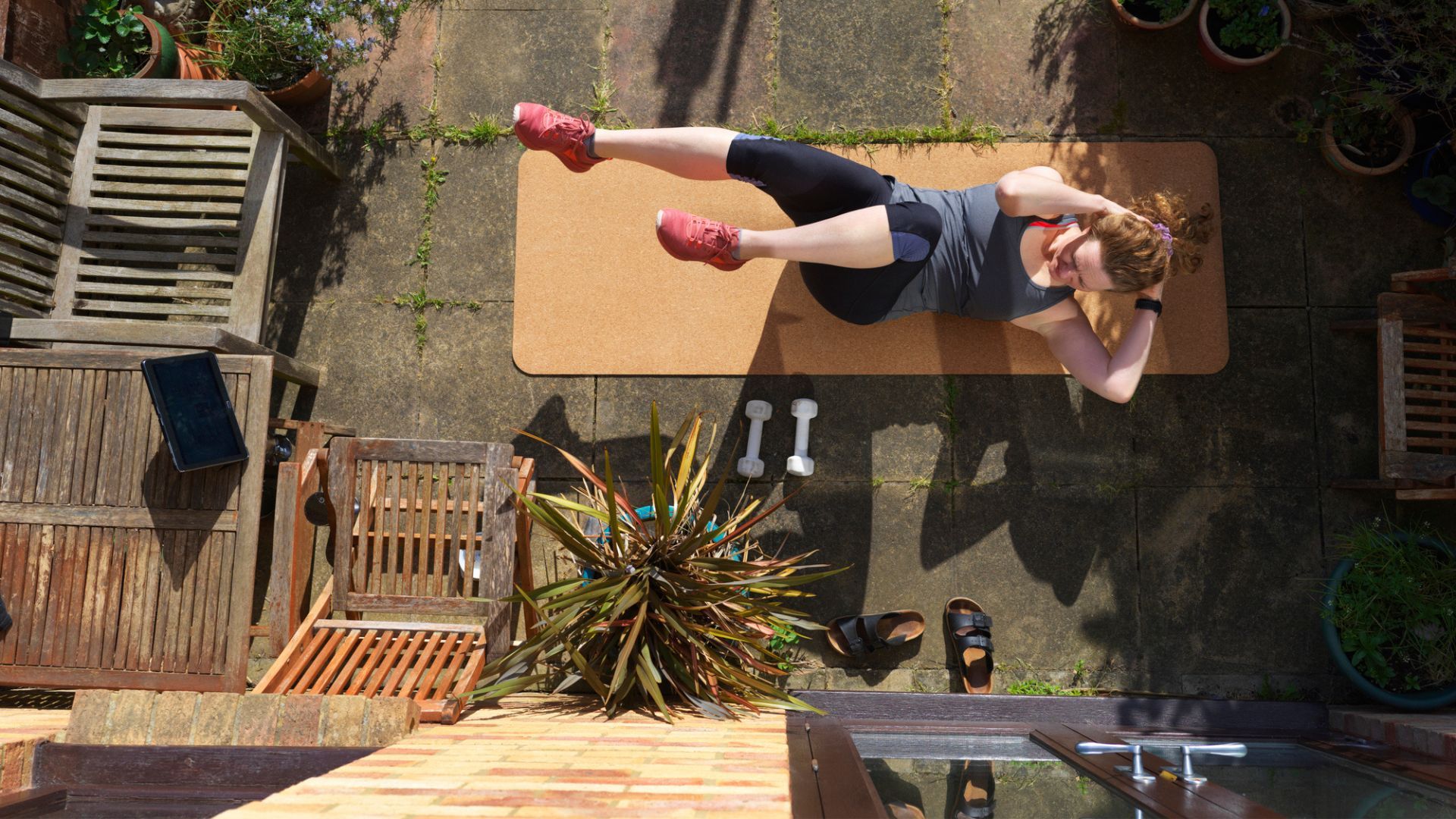 Woman exercising in garden with yoga mat and handheld weights