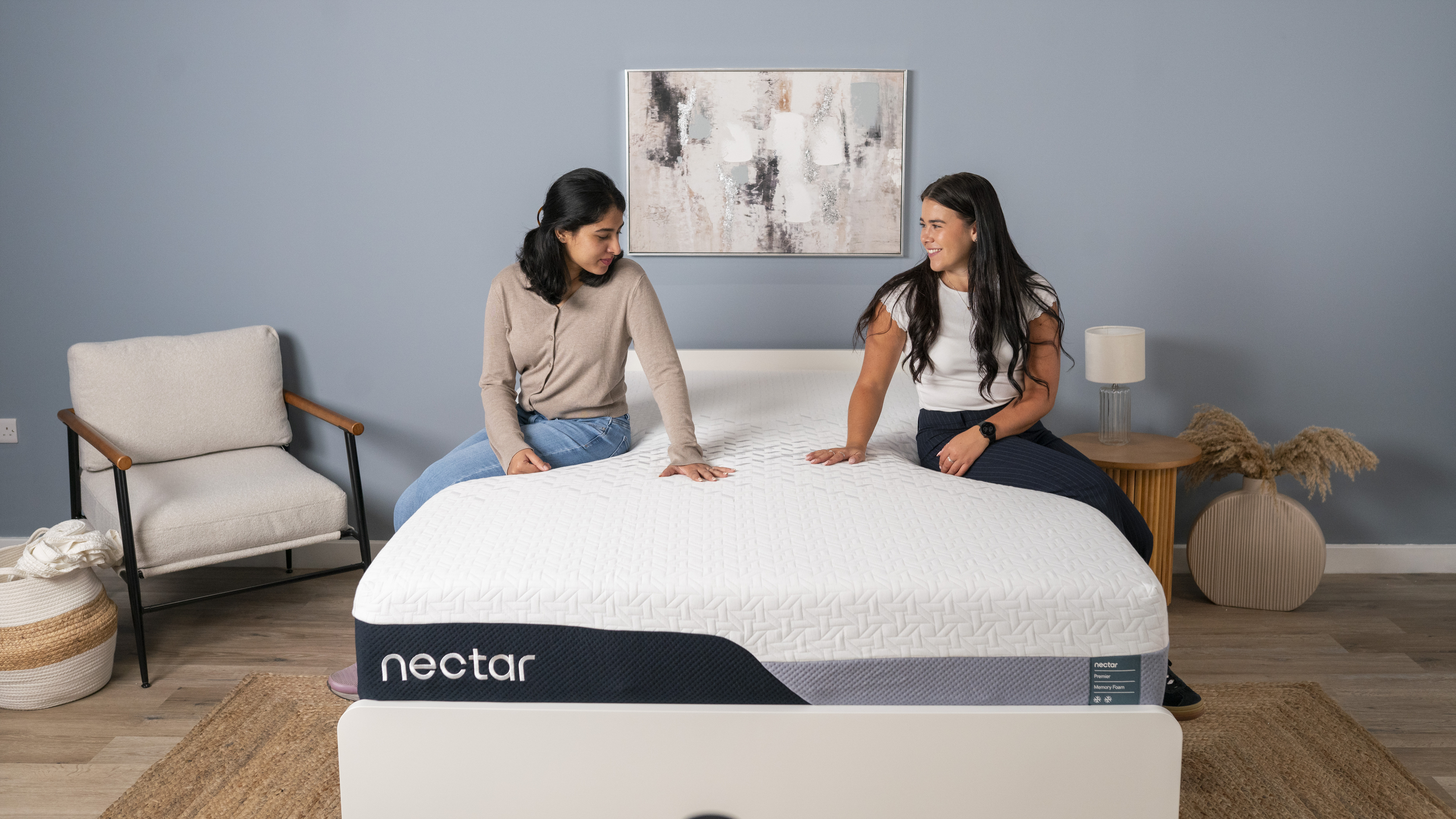 The image shows two women sat on the Nectar Premier Memory Foam Mattress