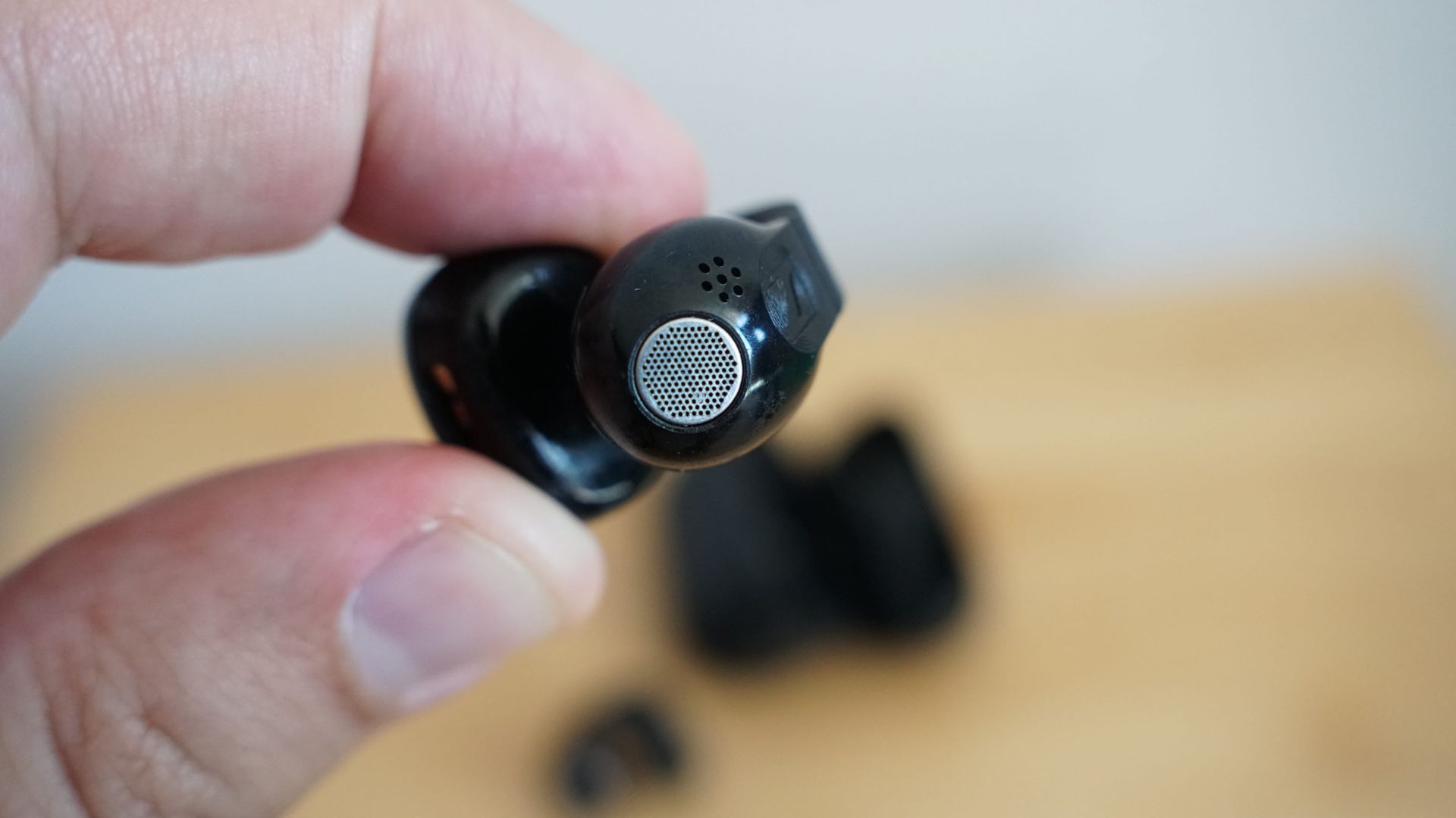 Sennheiser's Accentum Clip held in a hand, over a wooden table, with the case visible
