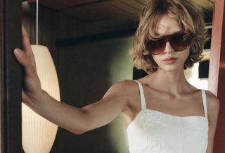 A Zara model wearing oversize sunglasses and a white sundress.