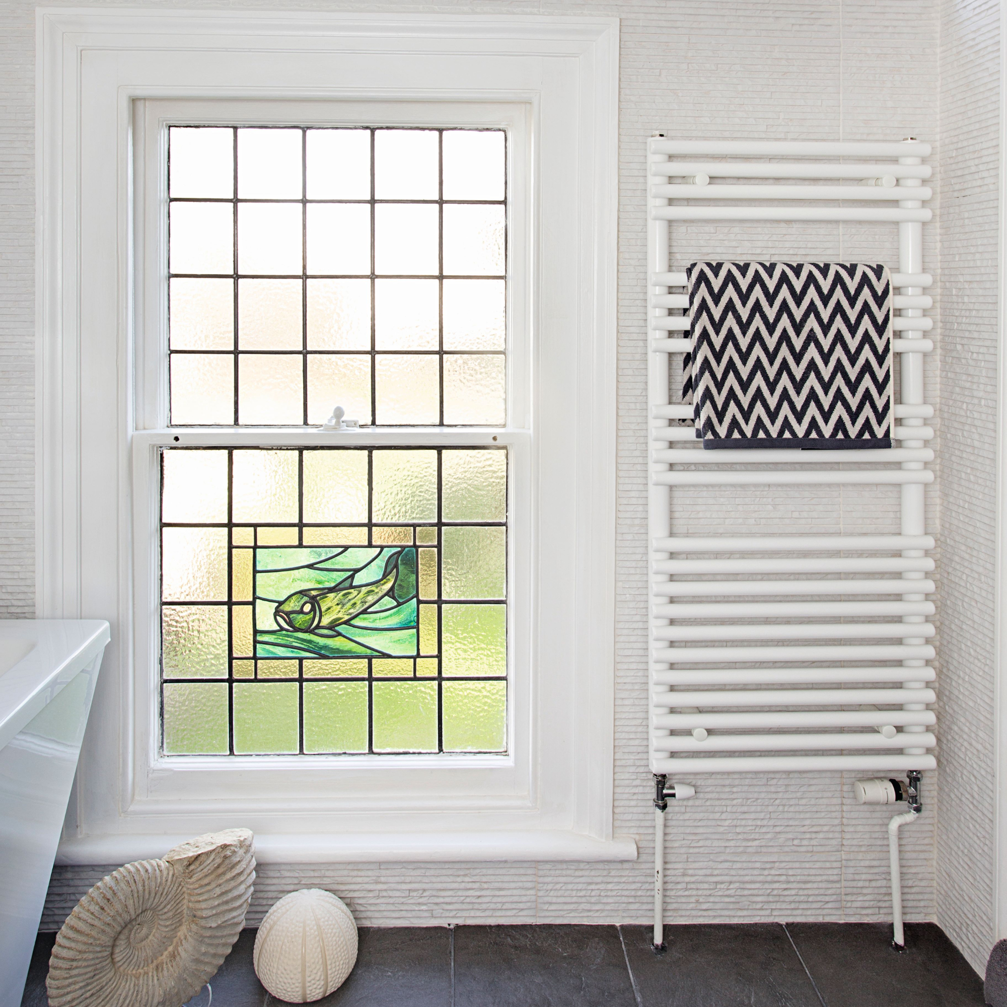 Stained glass bathroom window, heated towel rail with dark grey chevron towel, marine fossil ornament