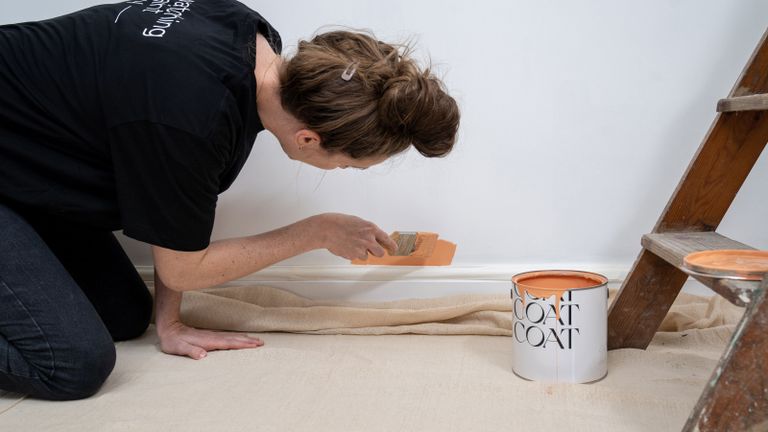 woman painting a white wall with coral paint