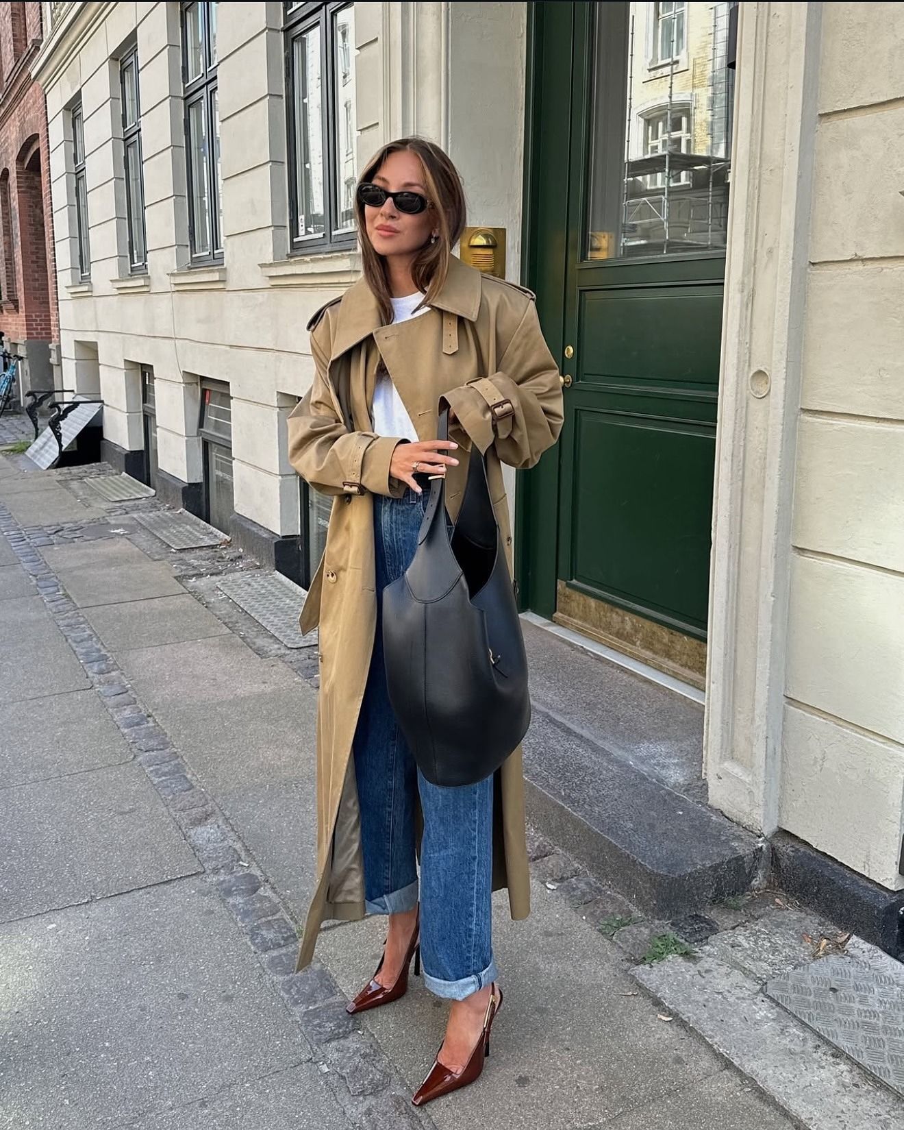 Influencer Felicia Akerstrom wears a white tee with cuffed blue jeans and a trench coat.