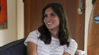 Kensi smiling on couch in striped shirt on NCIS: Los Angeles