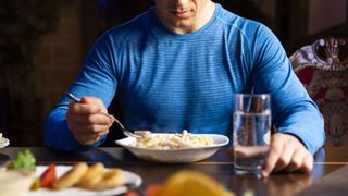 Man wearing gym clothes eating large bowl of pasta