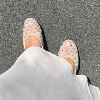 Woman wears rhinestone mesh Steve Madden flats with white slip skirt.