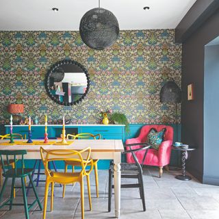 A dining room with a wallpaper-covered feature wall, mismatched dining chairs and several different sources of light