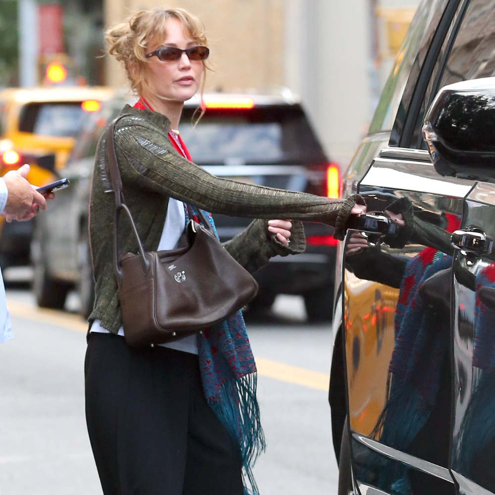 Image of Jennifer Lawrence today wearing a the leopard print mules trend 2026. She paired with with an olive cardigan, white T-shirt and black trousers. 