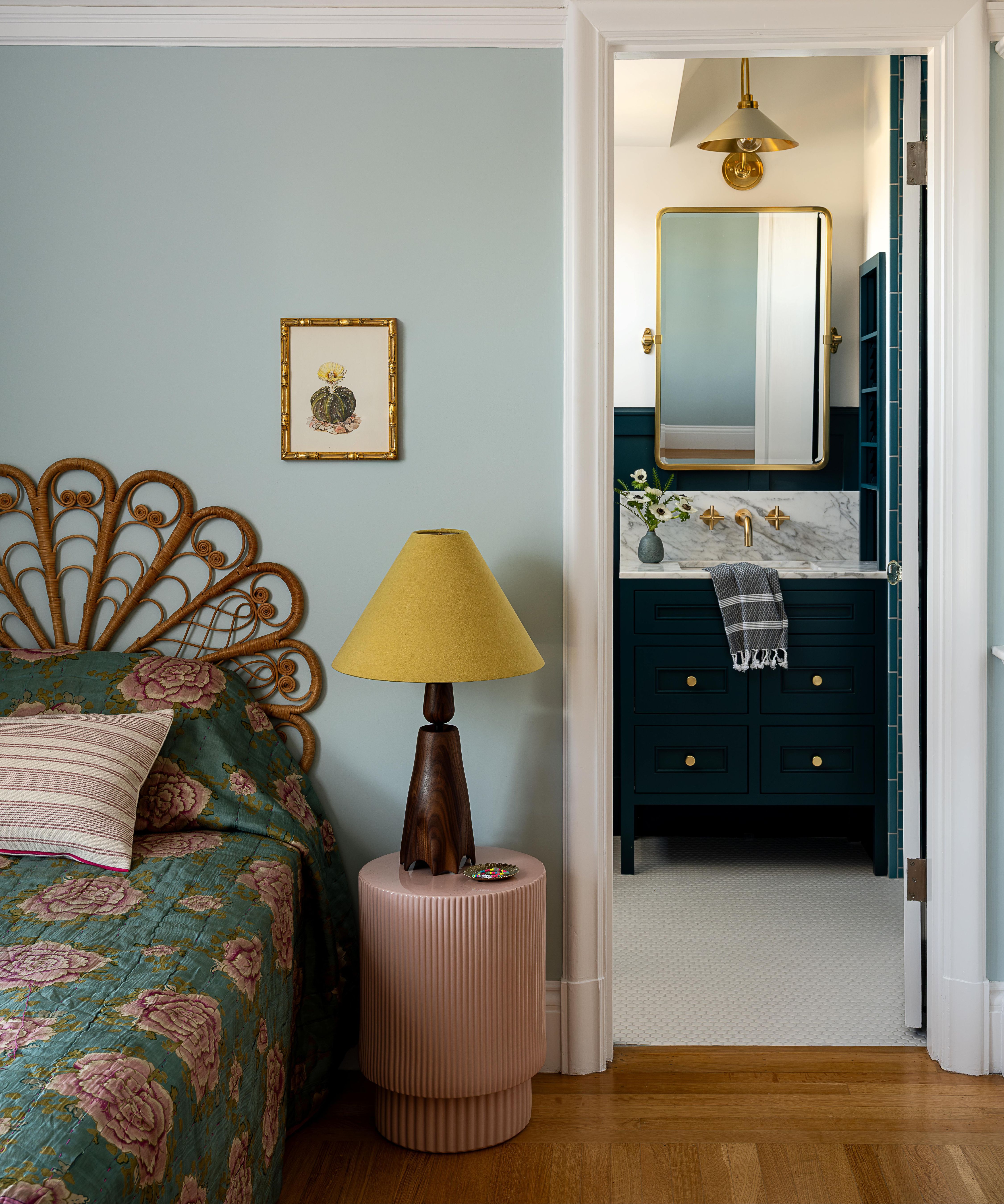 a soft blue painted kids room with a rattan sculptural headboard, a small pink drum shaped nightstand and a view through to an ensuite bathroom