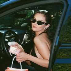 An image of Selena Gomez holding two Rare Beauty products and an Ulta shopping bag while posing in the open door of a car.