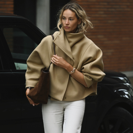 Woman wearing suede bag, funnel neck jacket, and white jeans.