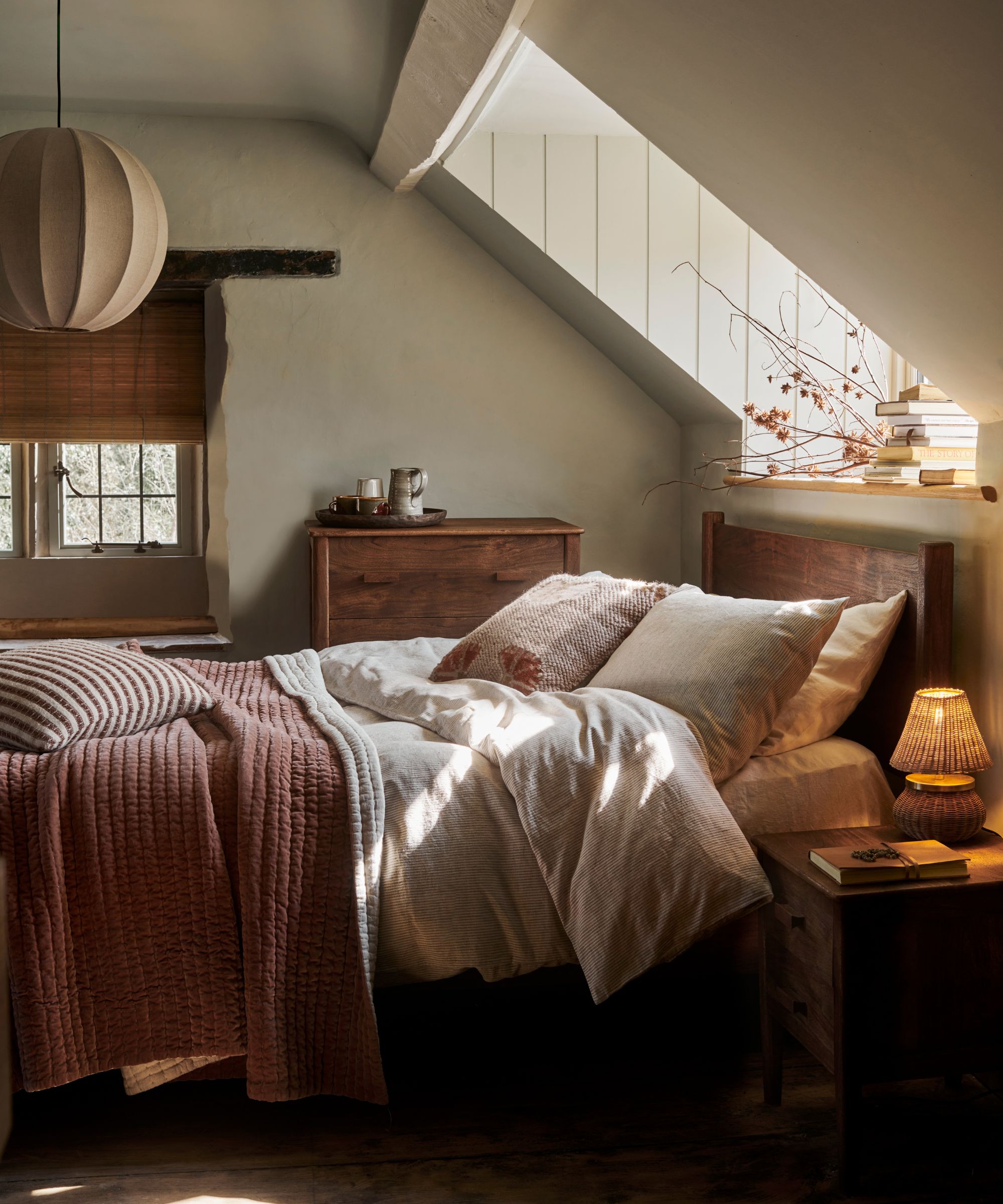 A cozy fall bedroom with a wooden bedframe and neutral bedding. A slanted roof with a skylight window above.