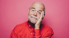Portrait of senior man in red shirt with head in hand against pink background