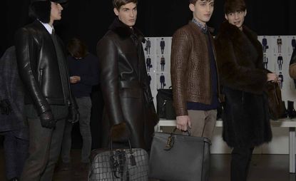 Four male models wearing looks from Fendi's collection. They are wearing trousers, shirts and sweaters in various colours along with brown and black coats and jackets made from leather and fur. One model is wearing gloves and a fur hat and another two models are holding bags with one wearing fur mittens