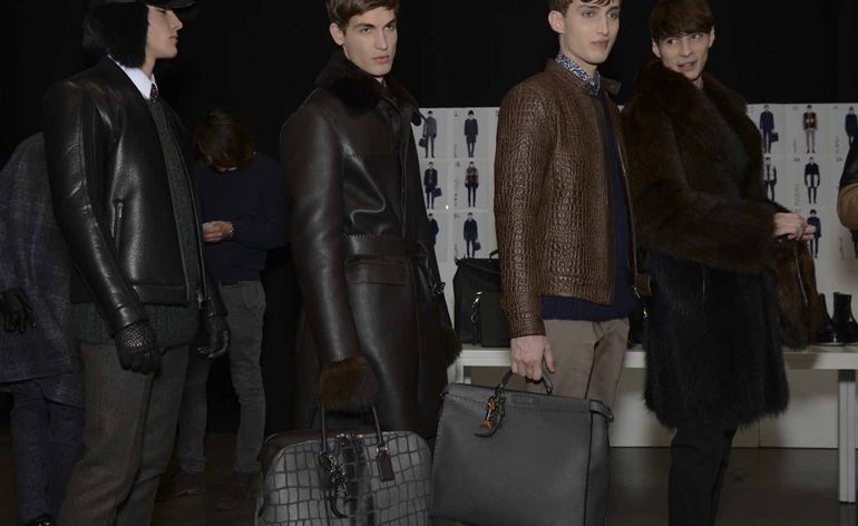 Four male models wearing looks from Fendi&#039;s collection. They are wearing trousers, shirts and sweaters in various colours along with brown and black coats and jackets made from leather and fur. One model is wearing gloves and a fur hat and another two models are holding bags with one wearing fur mittens