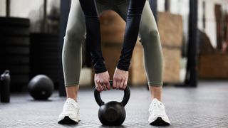 Person bending over in to bent over row gripping a kettlebell between their legs