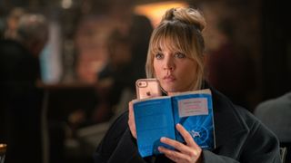 Kaley Cuoco as Cassie Bowden, holding a phone and a novel in The Flight Attendant Season 2 Episode 1