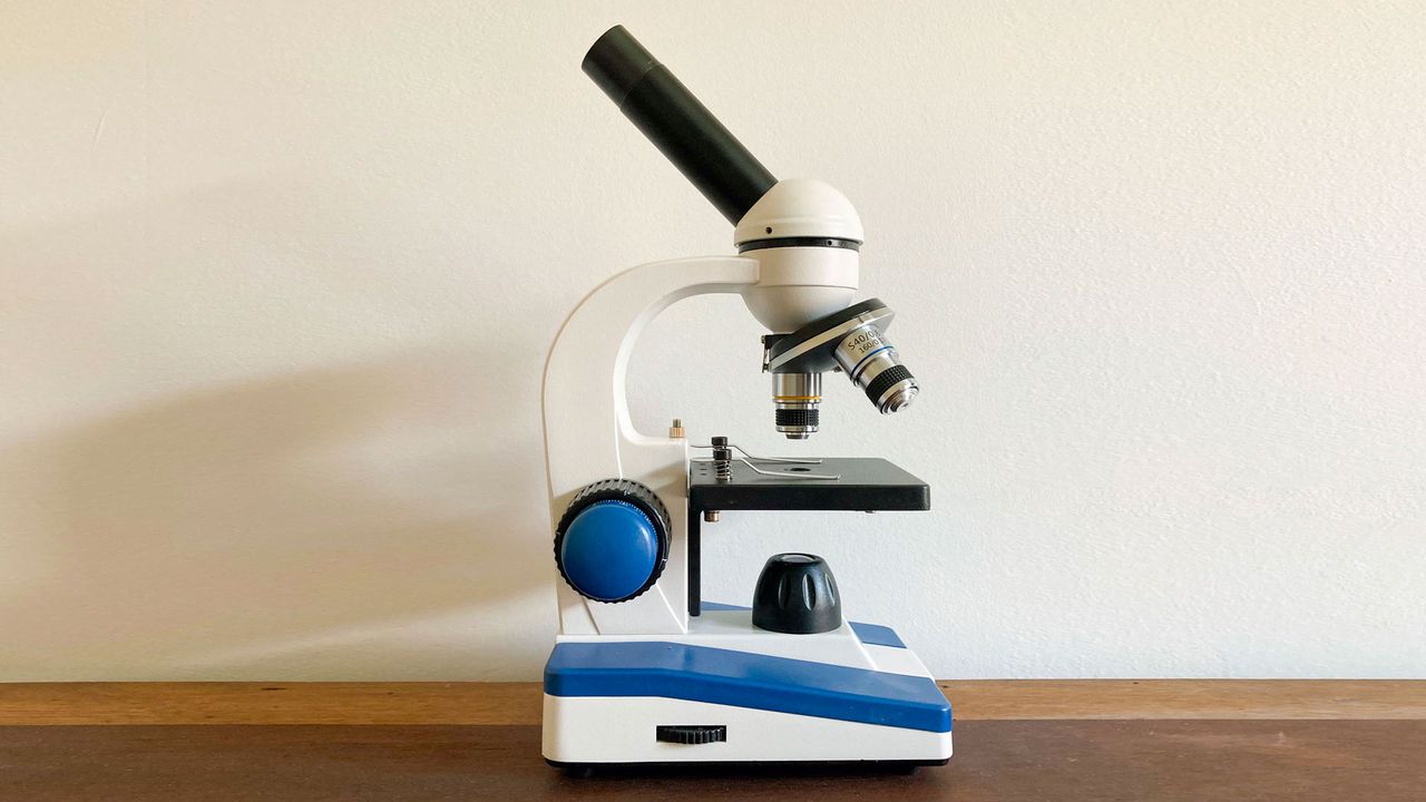 The amscope mc150c microscope placed on a walnut table against a beige wall