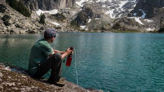 how to store your water filter over winter: man filtering water by mountain lake