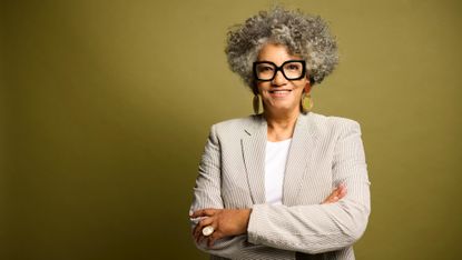 Senior businesswoman posing with her arms crossed against green studio background.