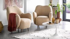 A living room with a pair of curved beige boucle armchairs with modern art on the wall and indoor tree
