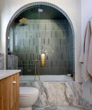 Bathroom with green glossy subway tiles in the shower and marble slabs on the walls and floors