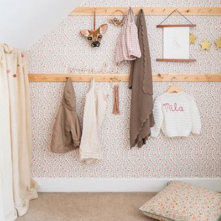 a childs room with floral wallpaper and two long peg rails for storage