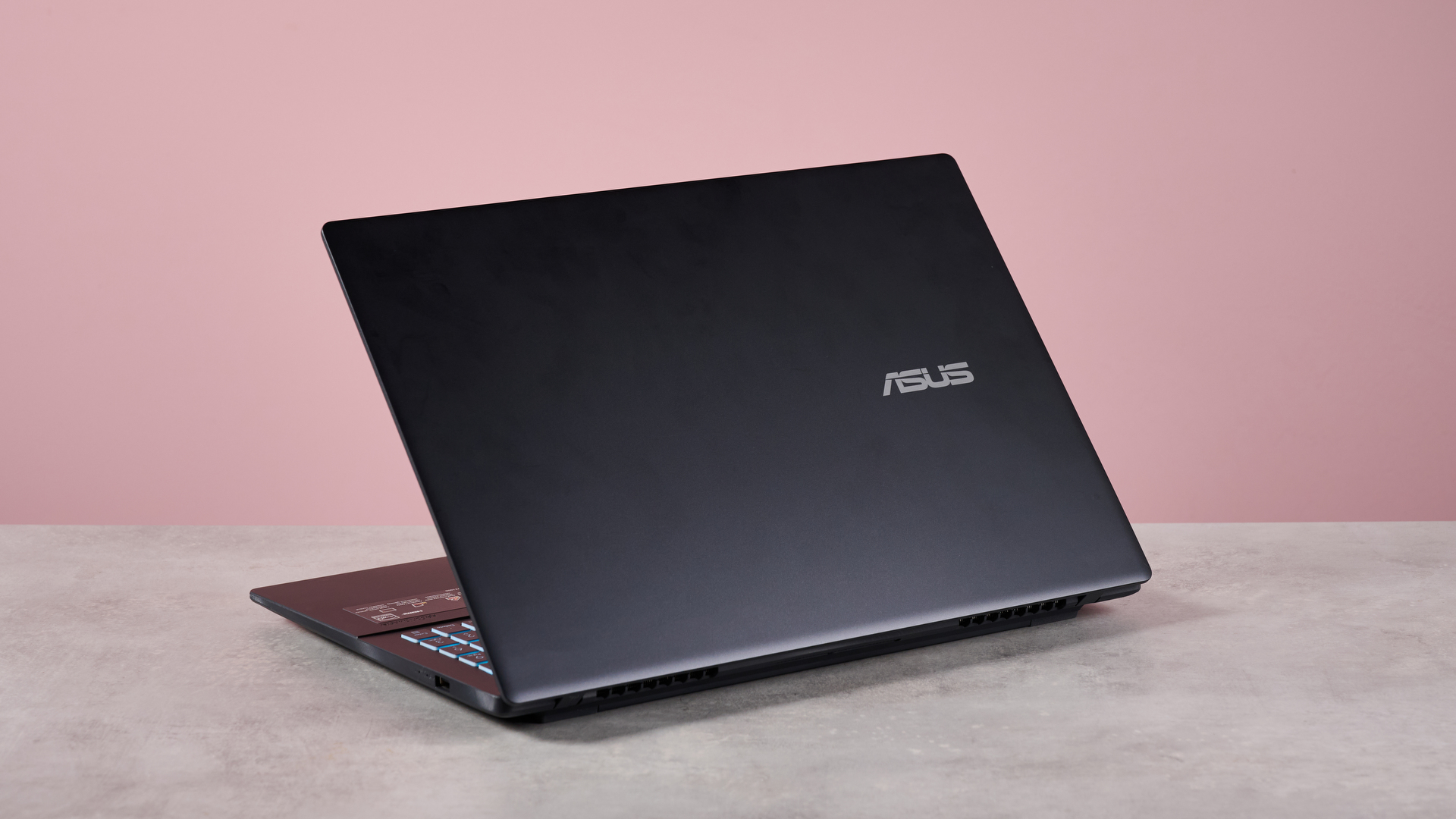 Rear three-quarter view of Asus V16 open on desk with pink wall in background
