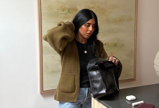 @monikh wearing a green Khaite sculpted cashmere cardigan with jeans and a black tote bag.