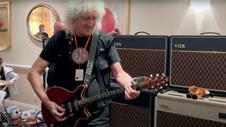 Brian May playing guitar with a backdrop of amps