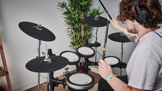 Man plays a Yamaha electronic drum set with a plant in the background