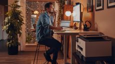 A man is sitting at his home office desk, using a HP laptop and monitor.