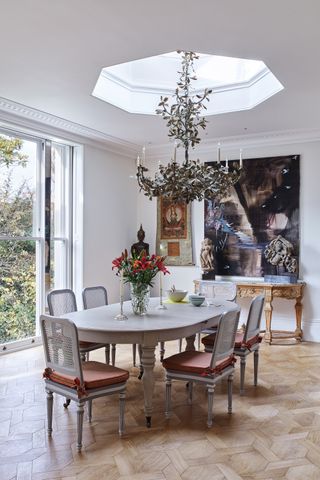 Octagonal shaped skylight and metal leaf design chandelier over dining room with classic dining table and chairs painted white and modern art on wall