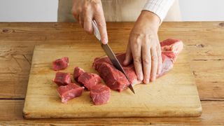 woman chopping a slab of meat on a wooden chopping board