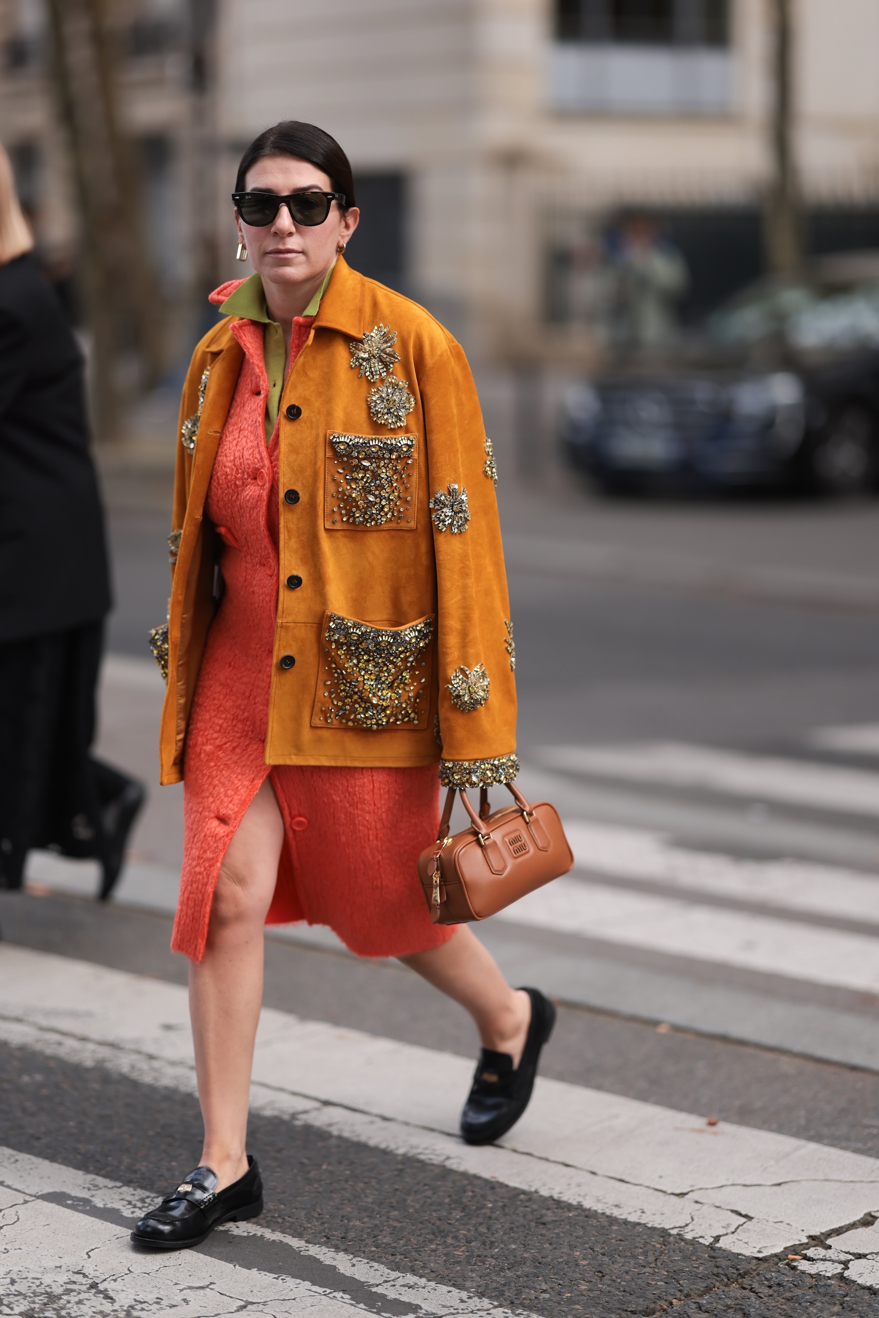 PARIS, FRANCE - OCTOBER 01: Alessandra Airo is seen wearing sunglasses with a dark Havana frame from Ray-Ban, several earrings, and an outfit from Miu Miu, consisting of a whiskey-colored embroidered suede jacket over a knee-length peach-colored buttoned mohair jacket, underneath a green polo shirt, a small rectangular cognac-colored “Arcadie” bag, and black leather loafers before the Miu Miu Womenswear Spring/Summer 2025 Show as part of Paris Fashion Week on October 01, 2024 in Paris, France. (Photo by Jeremy Moeller/Getty Images)
