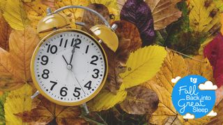A yellow alarm clock lying amongst autumn leaves with a blue 'Fall Back into Sleep' Tom's Guide logo