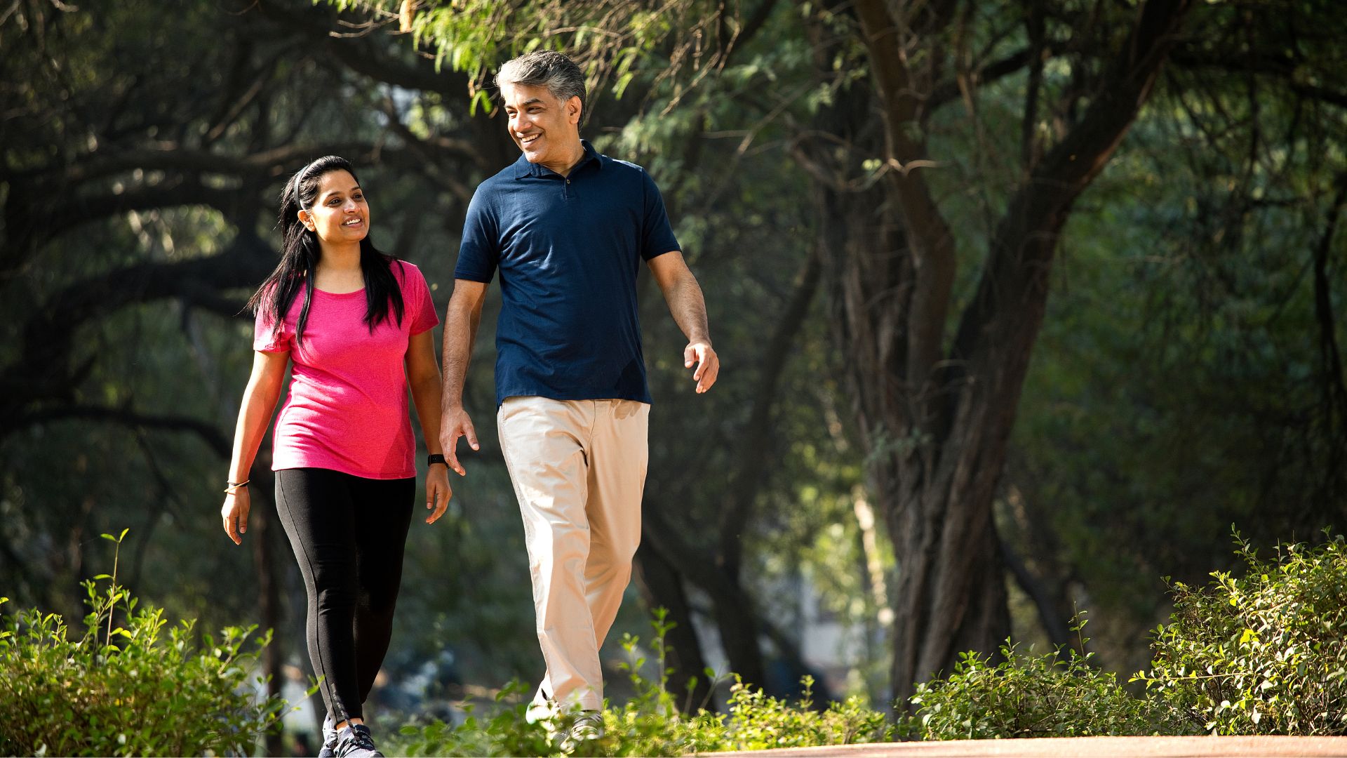 A couple go for a morning walk through a sunny park.