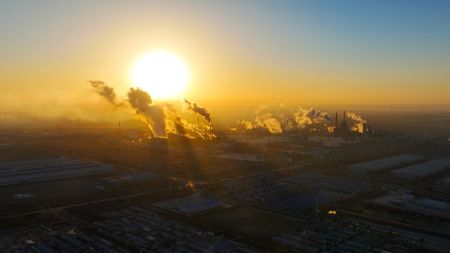 A large, yellow sun is pictured shining close to the horizon over an industrial region of China as smoke from industry pours into the air to reflect the light.