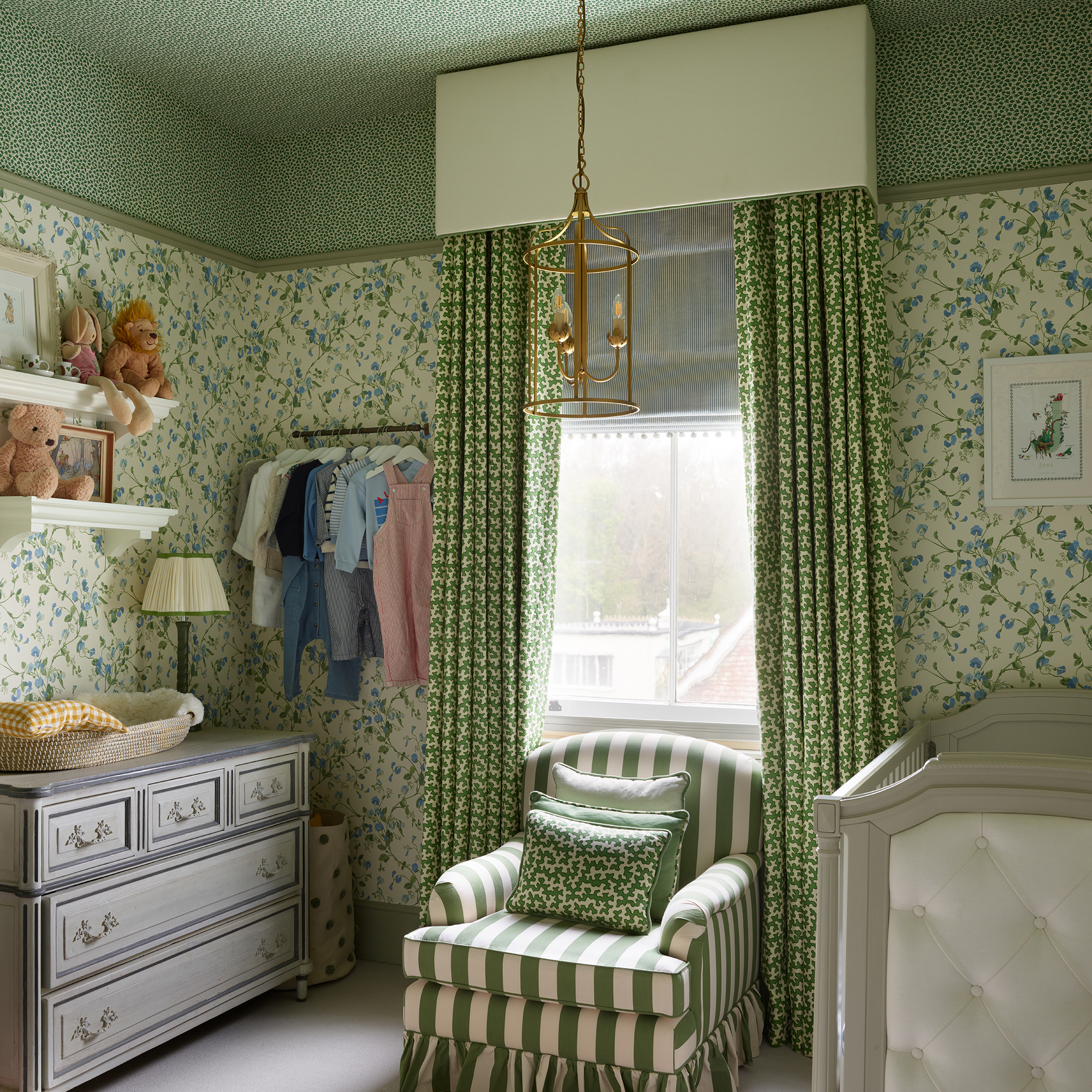 Nursery with green floral wallpaper and gree papered ceiling, green patterned curtains and striped armchair
