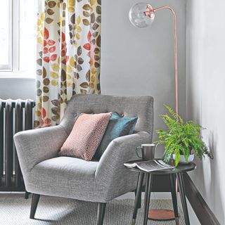 A grey armchair paired with a copper floor lamp on top of a grey carpet