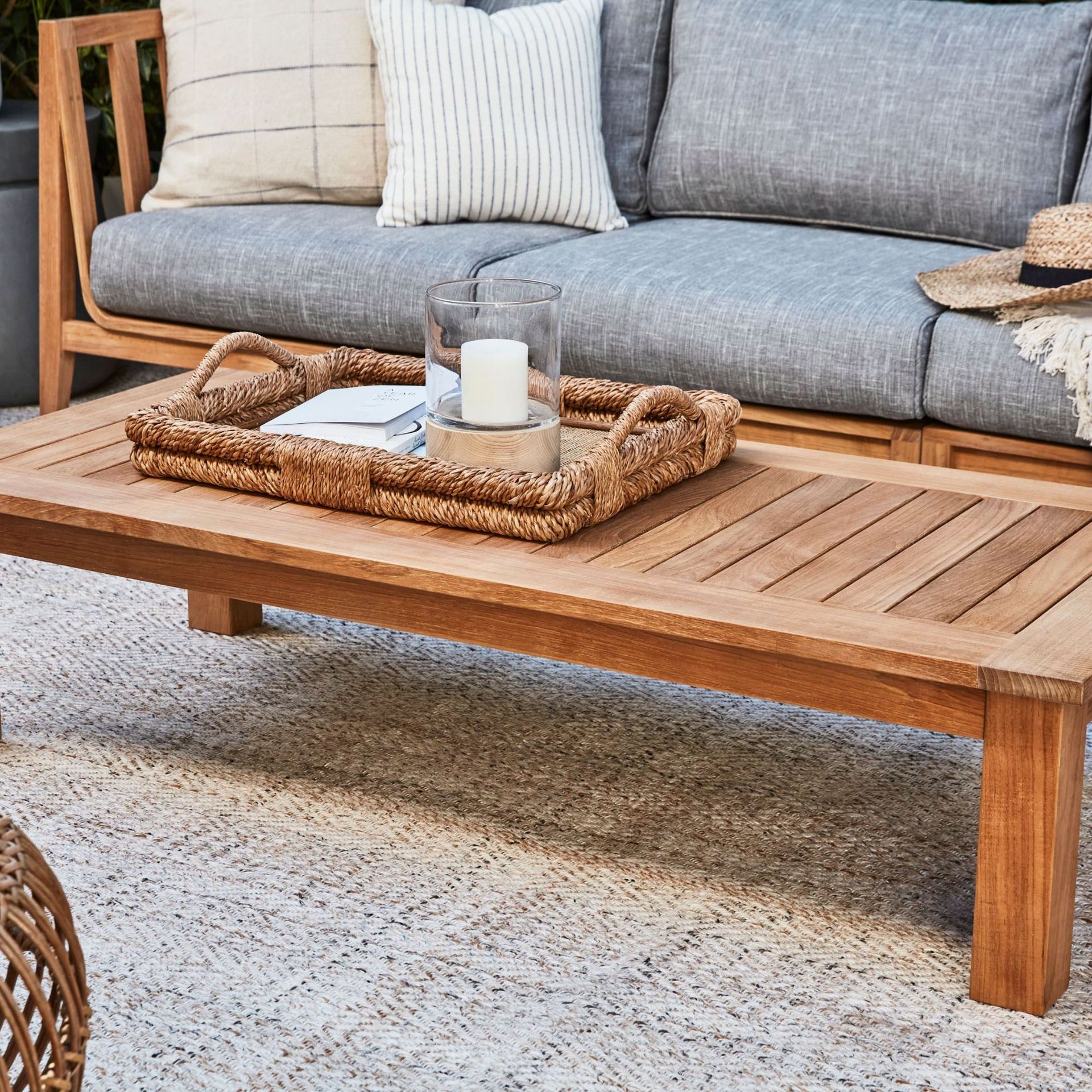 Teak Outdoor Coffee Table on a rug in front of a gray sofa.