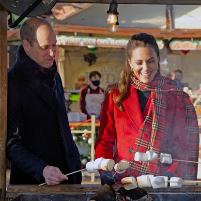 Kate Middleton wearing a red plaid scarf and red coat roasting marshmallows with Prince William outside