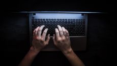 Person types on laptop in the dark