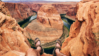 perspective view of mature man sitting with feet hanging over edge of cliff at Horseshoe Bend canyon