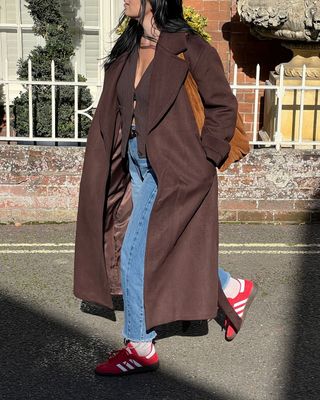 the best trainers for winter: @claudia_berresford wearing red suede trainers with jeans and long coat