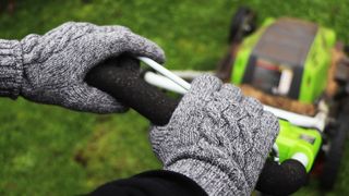 Gardener mowing the lawn wearing grey woolen gloves